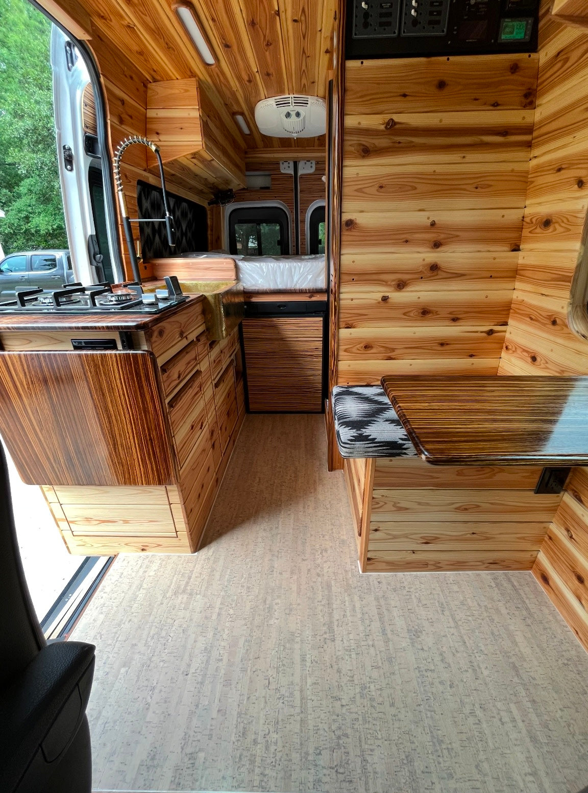 Inside an RV rental: a warm, custom wooden interior with kitchen, bed, and dining nook, ready for your road trip.