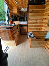 Inside an RV rental: a warm, custom wooden interior with kitchen, bed, and dining nook, ready for your road trip.