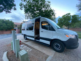 Experience comfort: This white rv rental camper van is parked at an RV site with its side door open, showing the equipped interior.