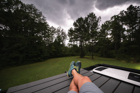 Relaxing on an RV rental with legs propped up, overlooking a forest under cloudy skies. Perfect outdoor retreat.