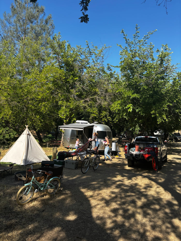 Enjoying the outdoors! An RV rental and tent are set up for camping, with a pickup truck and bikes nearby under sunny trees.