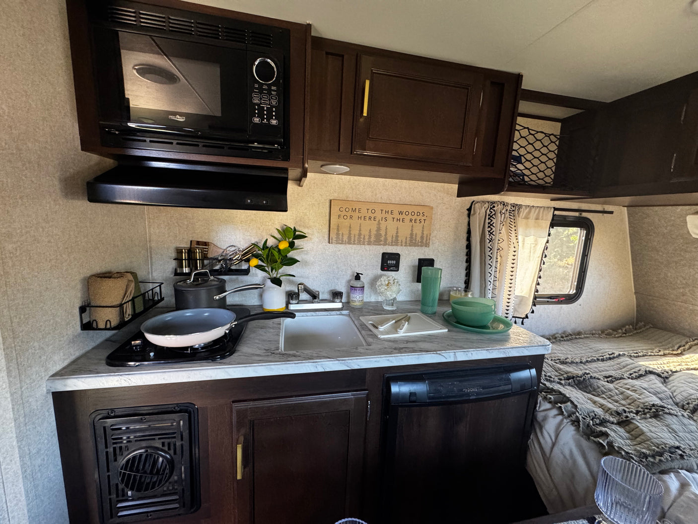 This RV rental boasts a functional kitchen with a microwave, stovetop, sink, and a comfortable sleeping area.