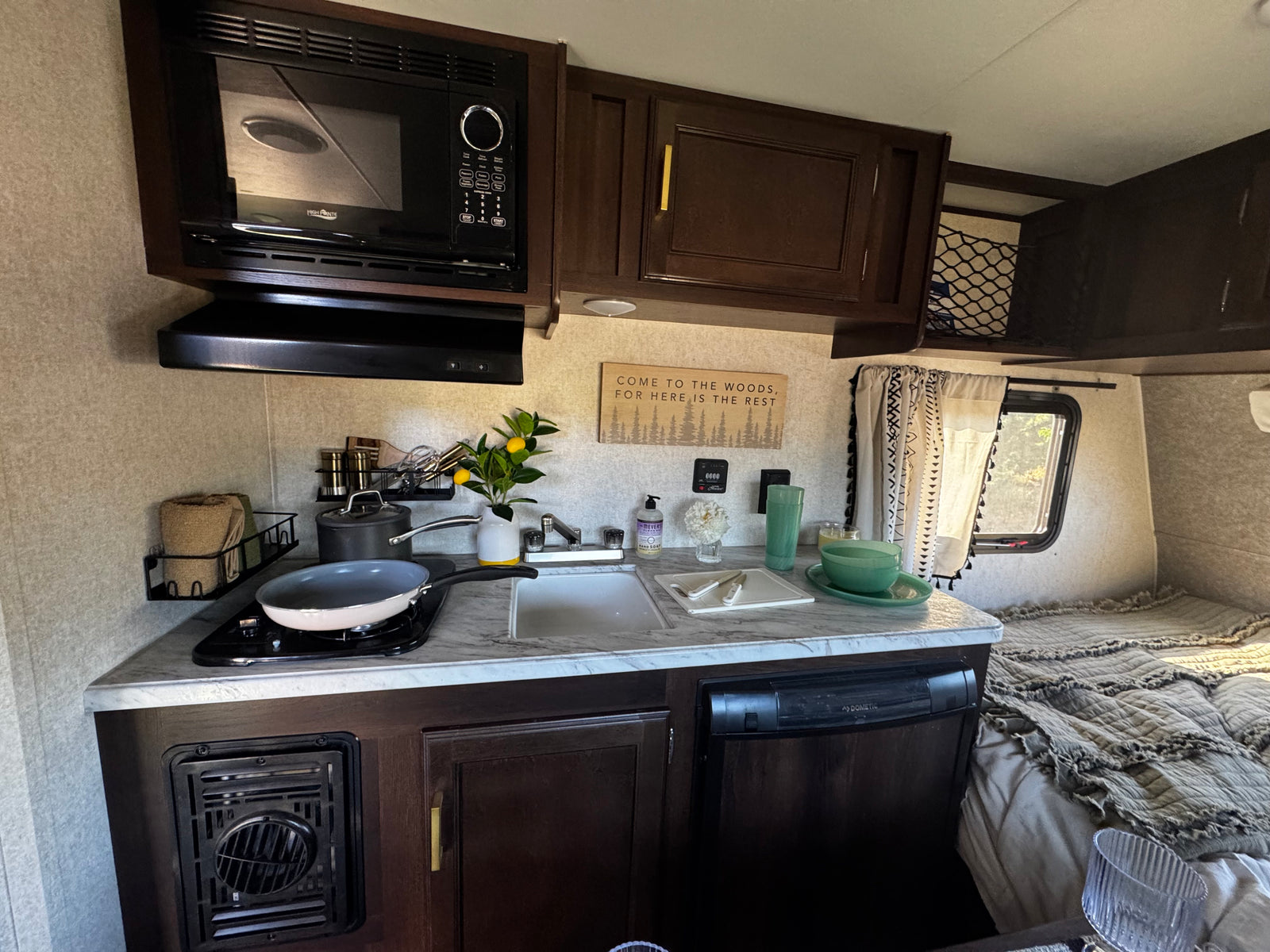 This RV rental boasts a functional kitchen with a microwave, stovetop, sink, and a comfortable sleeping area.