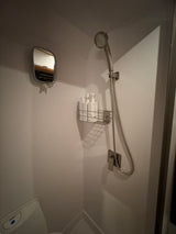 Compact RV rental bathroom: White shower stall, mounted mirror, shower head, toiletries, and toilet below. Efficient space.