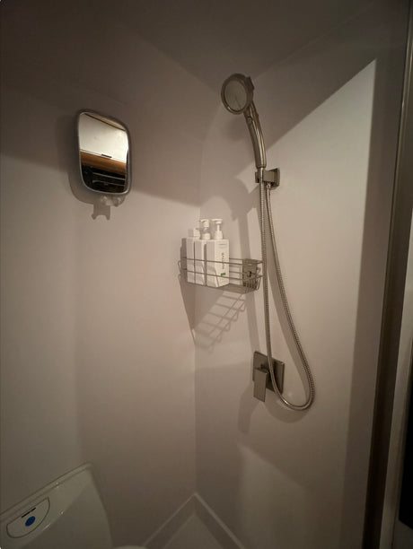 Compact RV rental bathroom: White shower stall, mounted mirror, shower head, toiletries, and toilet below. Efficient space.