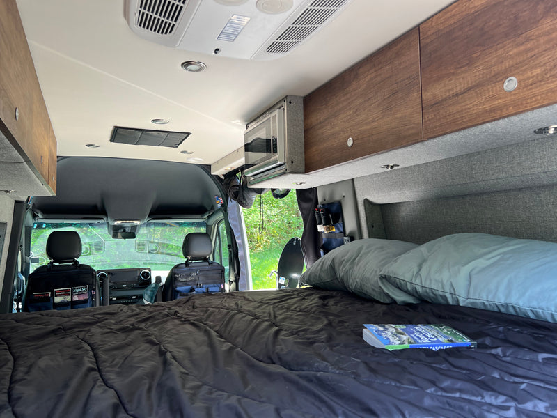Inside a well-equipped RV rental: a comfy bed, overhead storage, microwave, and front cab view. — photo 3