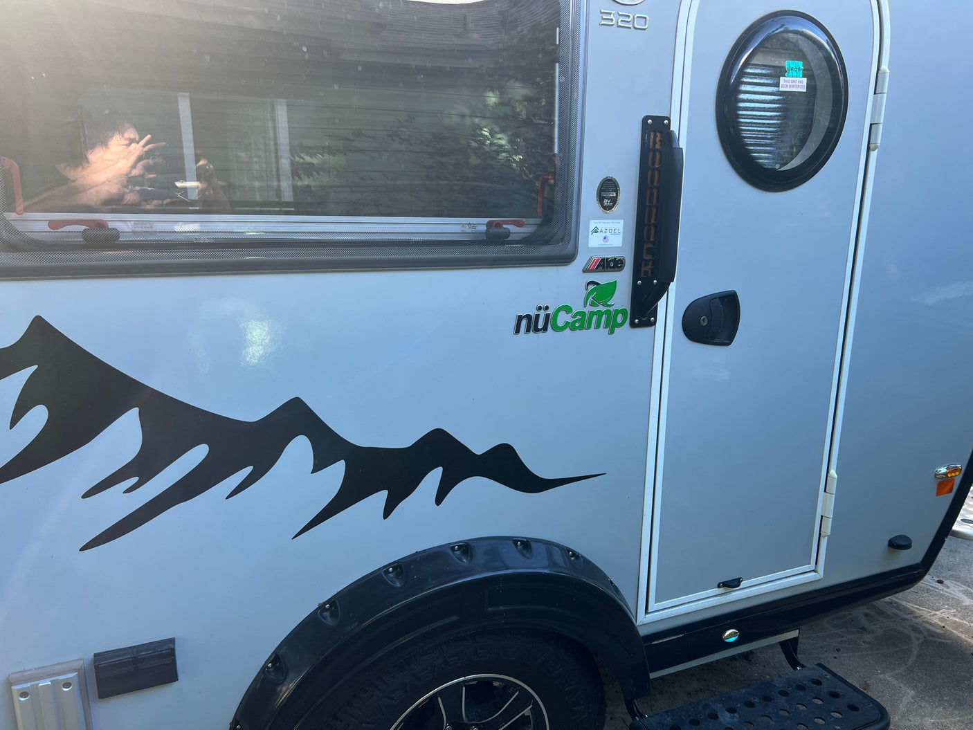Side view of a light gray nuCamp T@B 320 RV rental with a mountain graphic. Reflection of a person in the window.