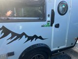 Side view of a light gray nuCamp T@B 320 RV rental with a mountain graphic. Reflection of a person in the window.