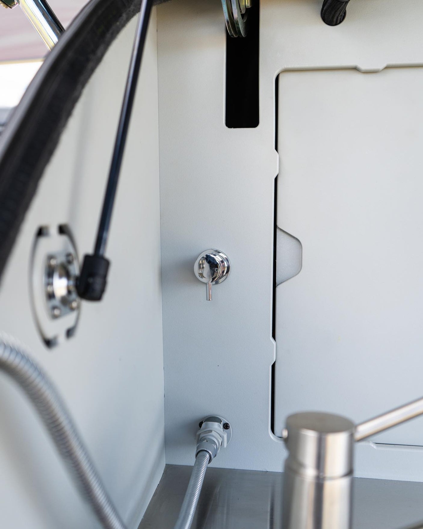 Inside an RV rental: a compact wash station with a chrome faucet, flexible hose, and stainless steel basin visible.