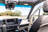 Modern Mercedes-Benz RV rental interior: dashboard, steering wheel, and open door view to scenic road trip ahead.