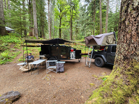 Forest campsite: an overland trailer & Jeep with rooftop tent/awning setup, an RV rental alternative for outdoor adventure.