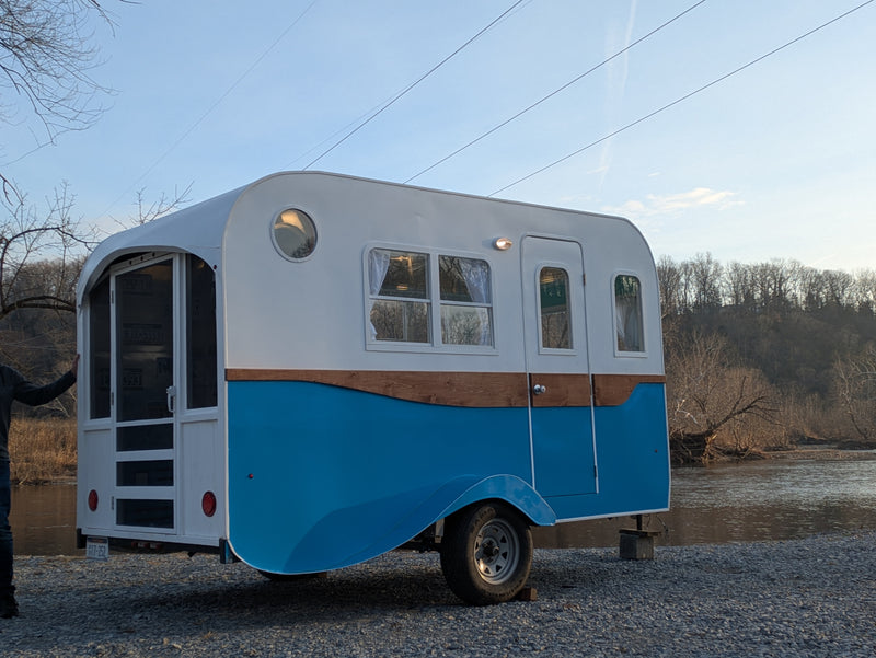 Small retro blue & white RV rental parked by a river under power lines. — photo 7