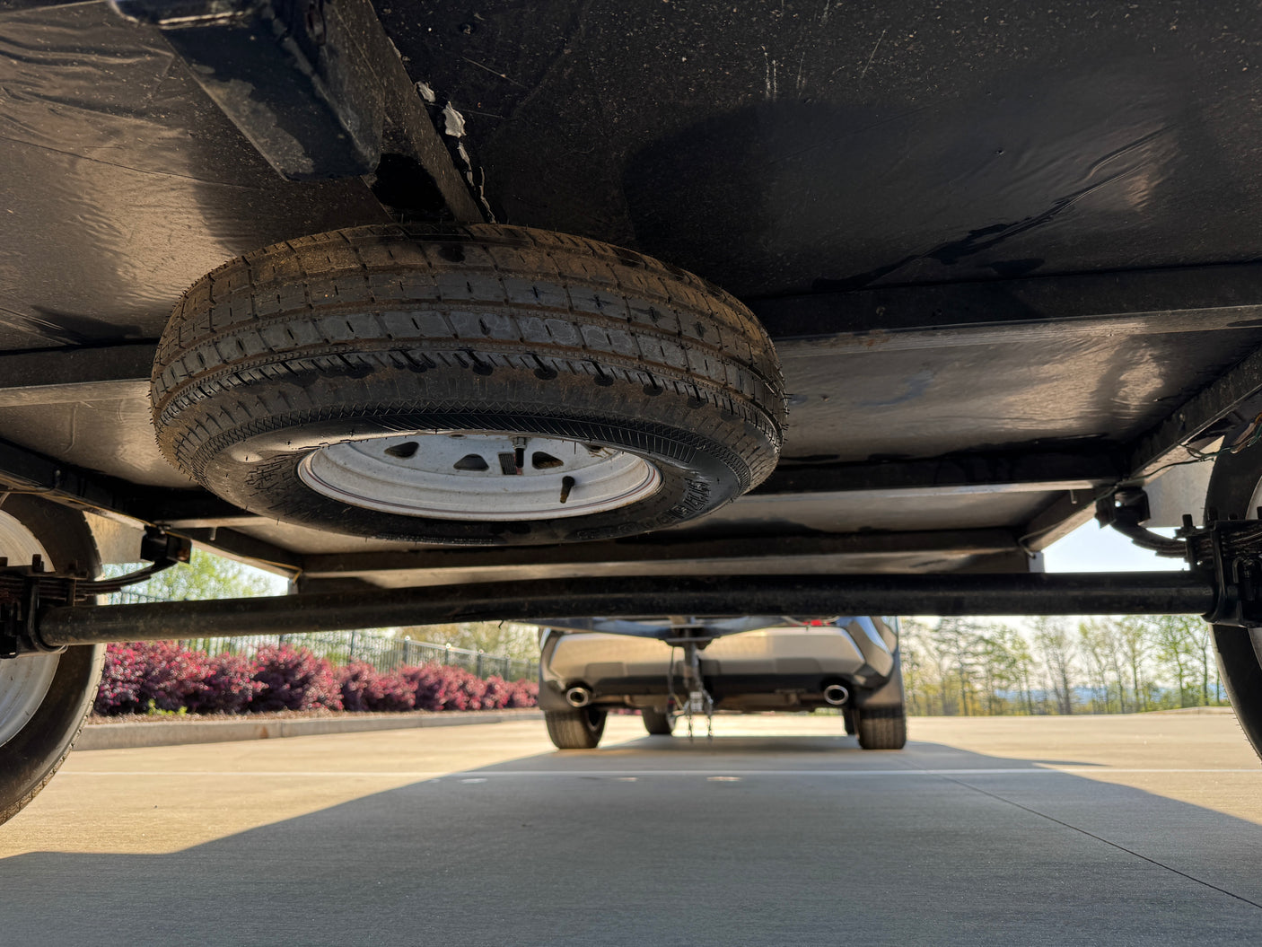 Underside view of an RV rental trailer with a mounted spare tire, hitched to a tow vehicle, ready for travel.