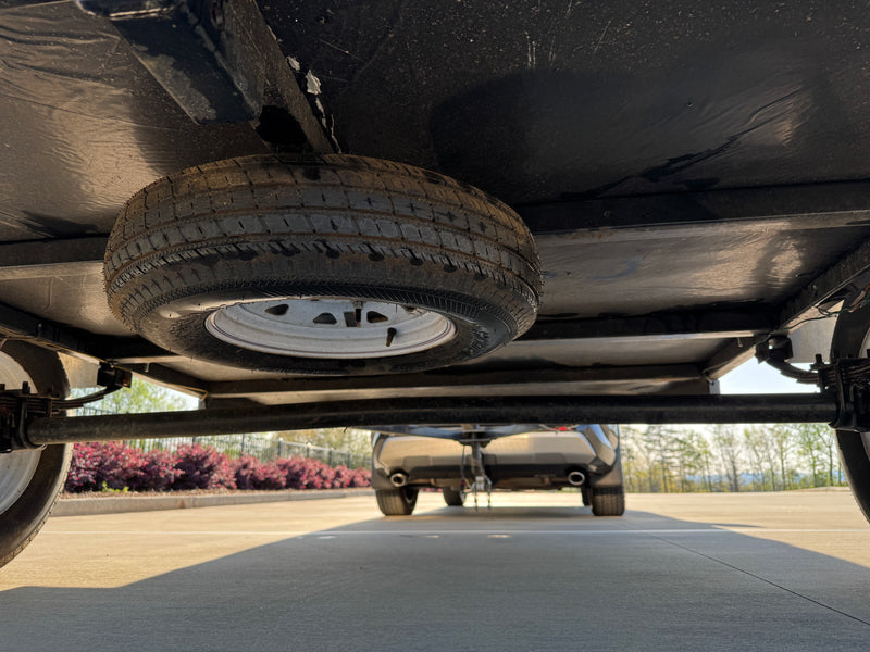 Underside view of an RV rental trailer with a mounted spare tire, hitched to a tow vehicle, ready for travel. — photo 6