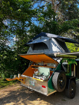 This RV rental teardrop trailer features a rooftop tent & outdoor kitchen, ready for camping in the woods.