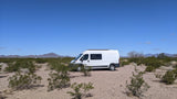 This RV rental camper van is parked amidst desert bushes with mountains in the background under a clear blue sky.