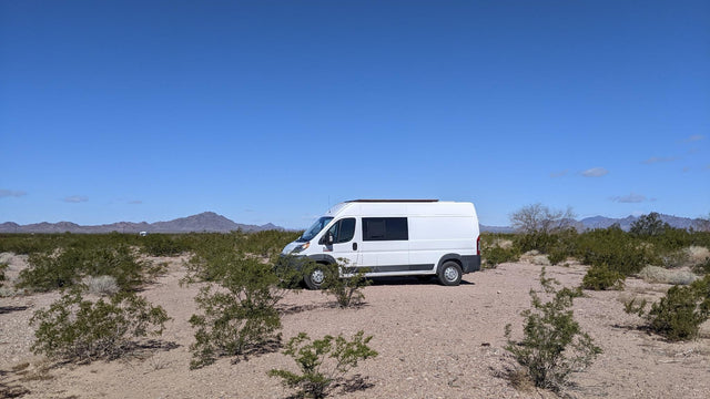 This RV rental camper van is parked amidst desert bushes with mountains in the background under a clear blue sky.