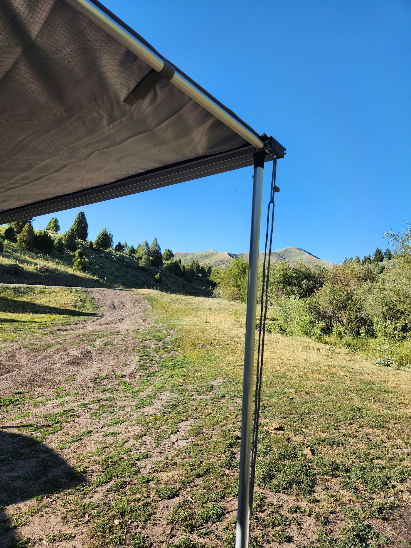 RV rental awning shades a sunny landscape with green hills, trees, and grassy fields under a blue sky. — photo 15