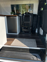 Inside an RV rental: a modern camper van with wood-look floors, kitchenette with fridge, flexible seating, and clear entry space.