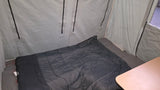 RV rental's compact interior: a dark sleeping bag on a gray bed, light fabric walls, and part of a wooden table.