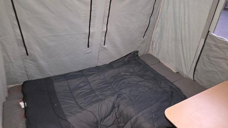 RV rental's compact interior: a dark sleeping bag on a gray bed, light fabric walls, and part of a wooden table. — photo 4