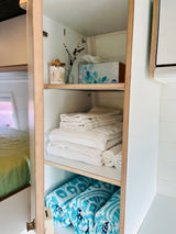RV rental amenities: Shelves filled with clean white towels, blue patterned beach towels, tissues, and cotton swabs.