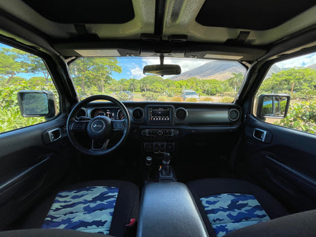 Interior of a rental Jeep Wrangler: dashboard, steering, blue camo seats & scenic mountain view. Ideal for your next RV rental adventure.