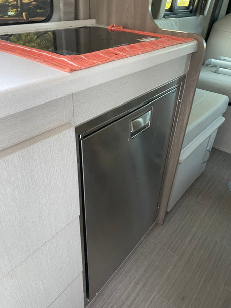Modern RV rental kitchen with cooktop, stainless fridge, and light wood cabinetry for compact living.
