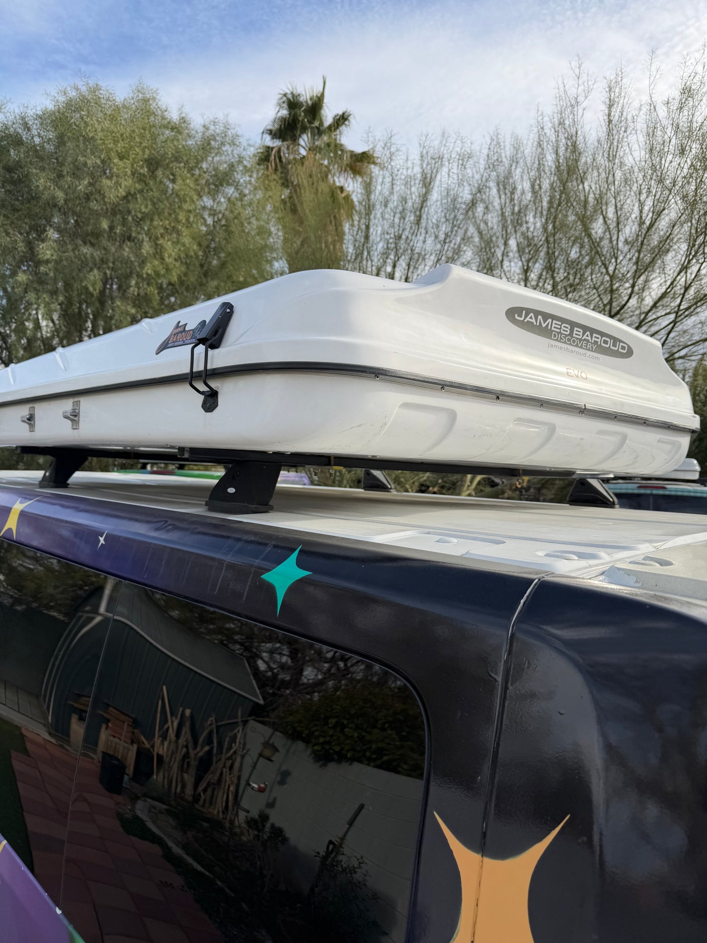 White James Baroud Discovery EVO rooftop tent mounted on a dark RV rental with custom decals, under a cloudy sky.