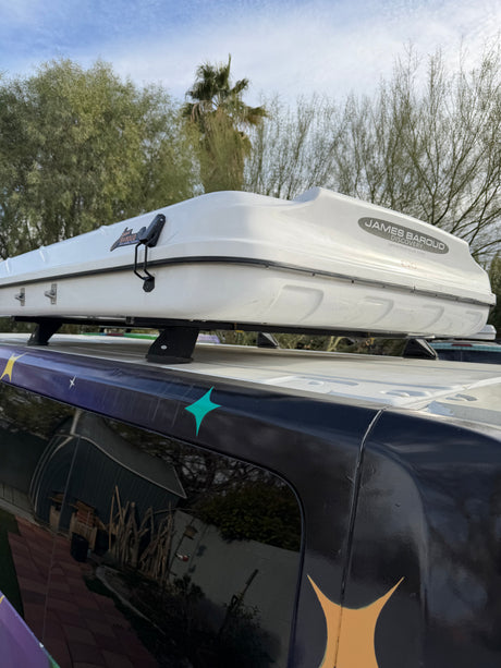 White James Baroud Discovery EVO rooftop tent mounted on a dark RV rental with custom decals, under a cloudy sky.
