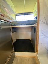 Cozy RV rental interior with a bed, under-bed storage, fridge, and stylish tiled wall.