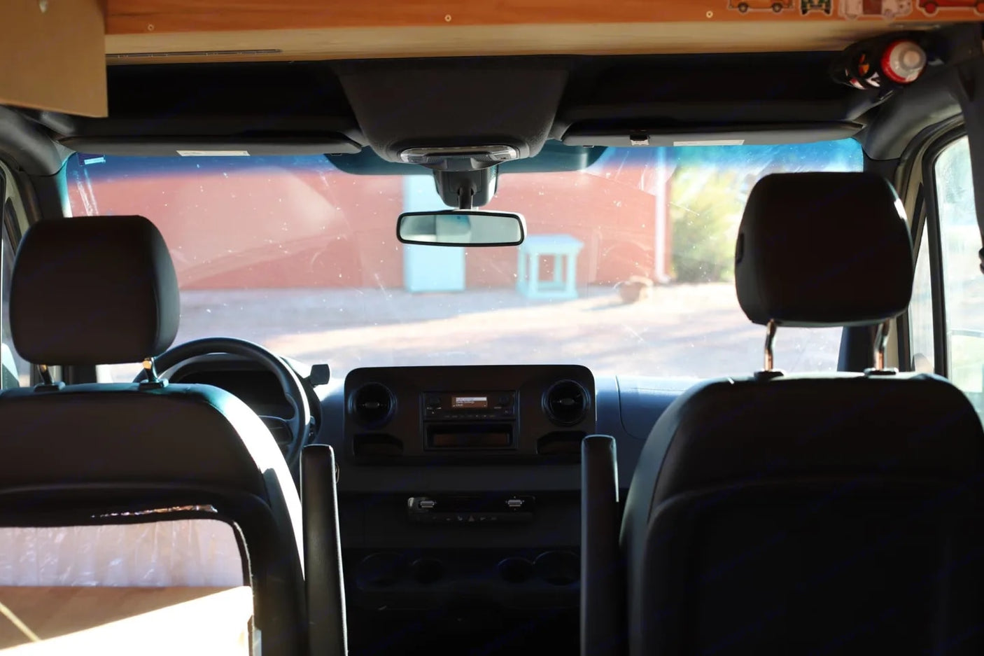 Inside an RV rental: Looking forward past front seats and dashboard to a bright outdoor view through the windshield, ready for travel.
