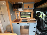 RV rental kitchen featuring microwave, sink, induction cooktop, fridge, light blue cabinets, bamboo accents. Shower and toilet visible on left.