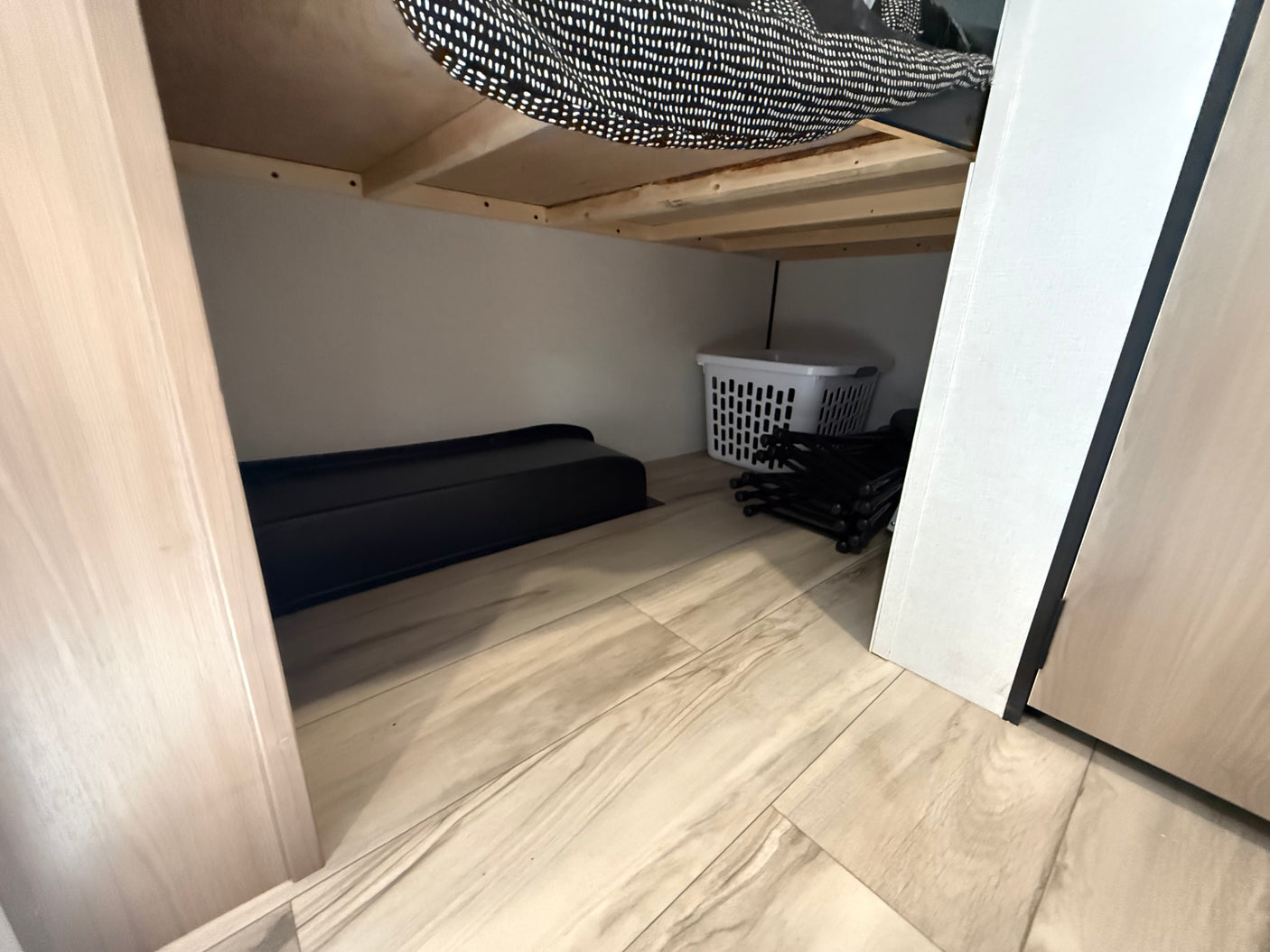 Efficient RV rental under-bed storage: black tray, laundry basket, & folded chairs on a wood floor.