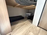 Efficient RV rental under-bed storage: black tray, laundry basket, & folded chairs on a wood floor.