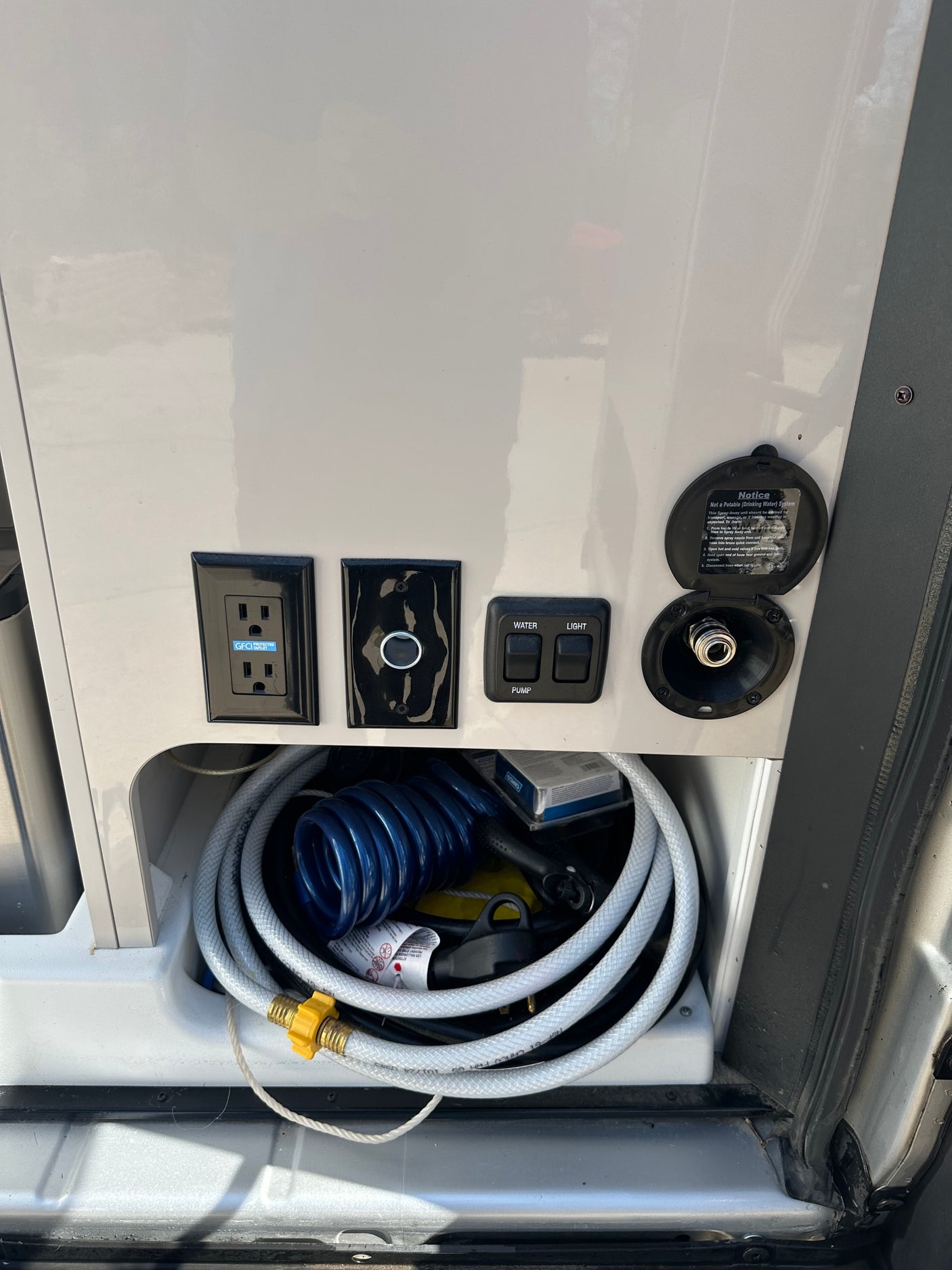 RV rental exterior utility panel with GFCI outlet, non-potable water connection, pump/light switches, and hoses.