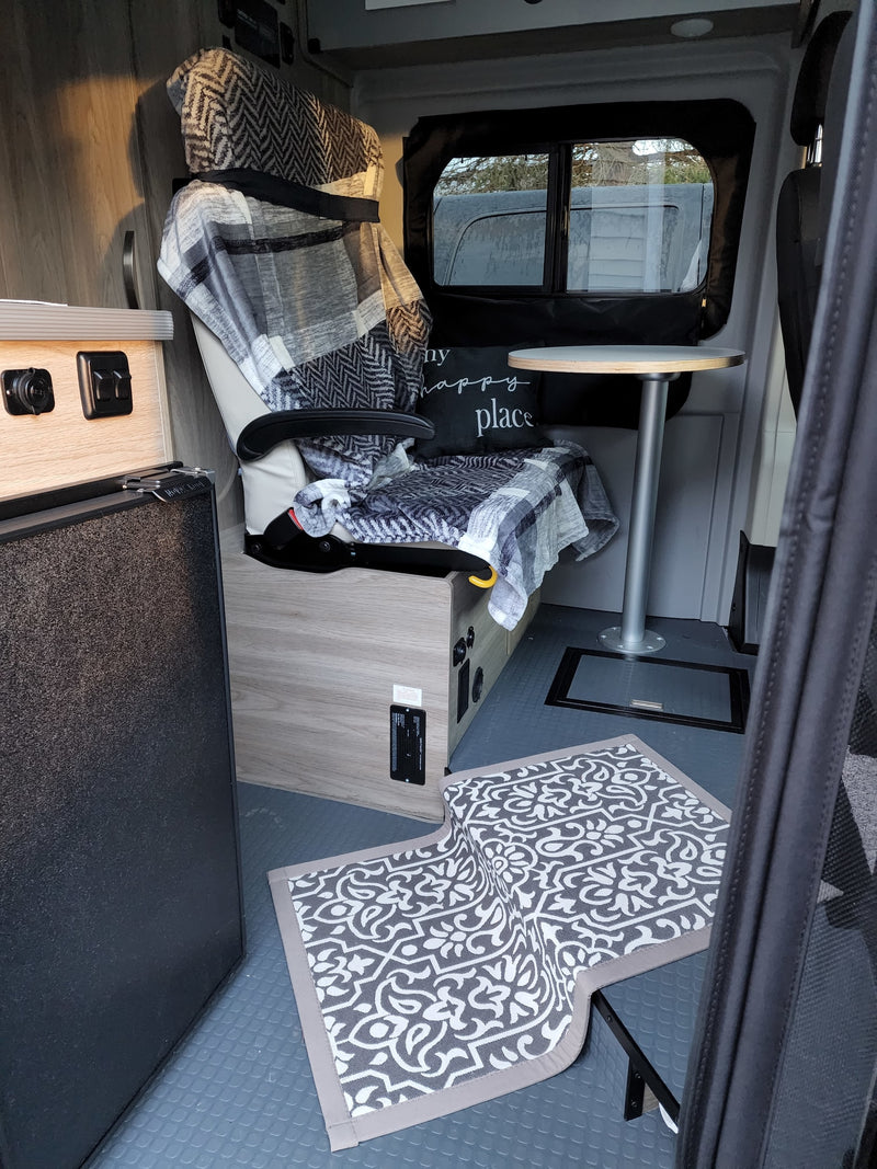 Inside a cozy RV rental: a comfy patterned chair with blankets, a small table, and a fridge on a textured floor. — photo 7