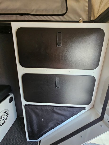 RV rental interior showing two black storage compartments with handles, a lower fabric pocket, and a speaker on a textured floor.