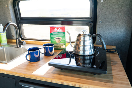 Enjoy morning coffee in this rv rental kitchen! Gooseneck kettle on induction cooktop, Melitta filters, sink, and blue mugs.