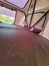 Inside an RV rental rooftop tent: a comfortable sleeping area with views of lush green trees, perfect for camping.