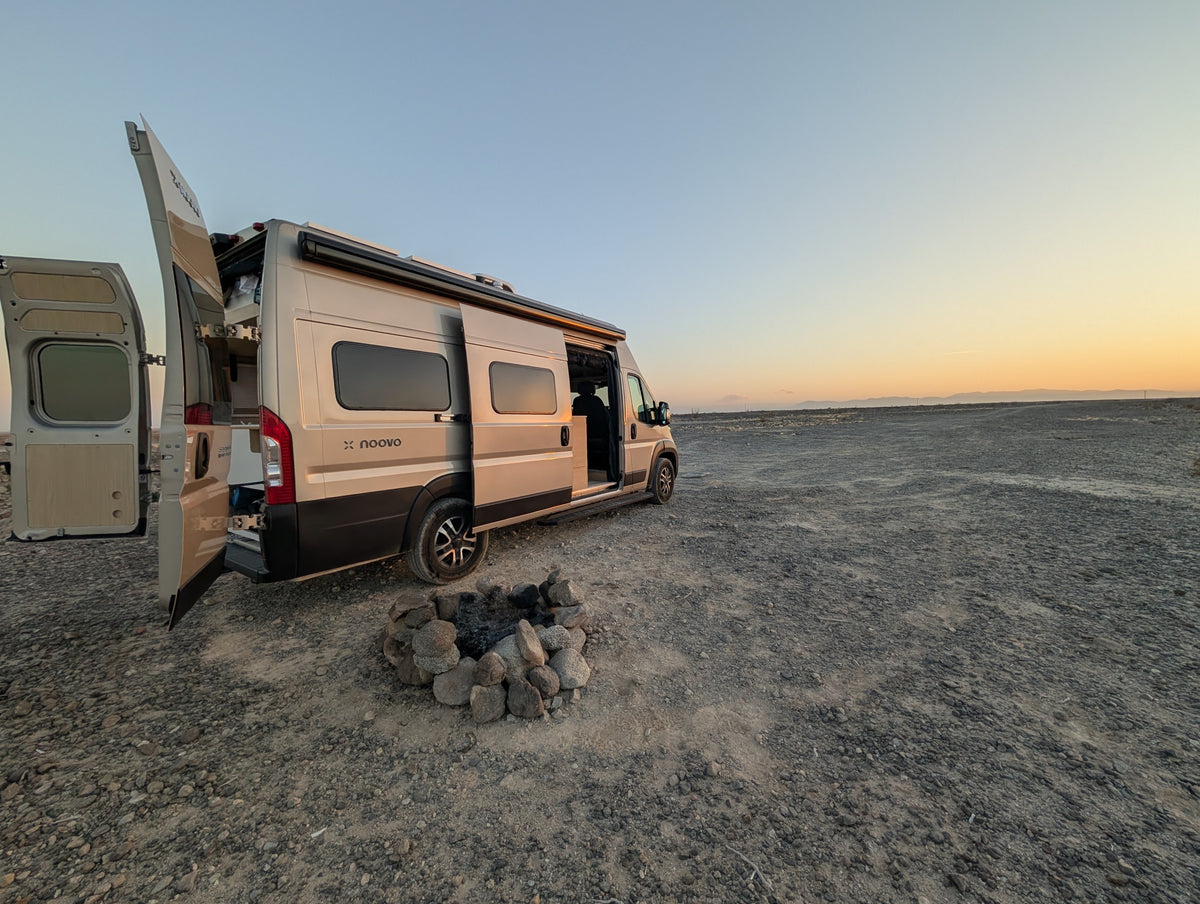 RV rental camper van with open doors, beside a rock fire pit on a gravel plain, under a fading sunset sky. — photo 9