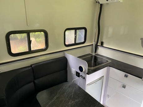 Modern RV rental interior: cozy dinette with black couch & marbled table, compact kitchen with sink & fridge, plus windows.