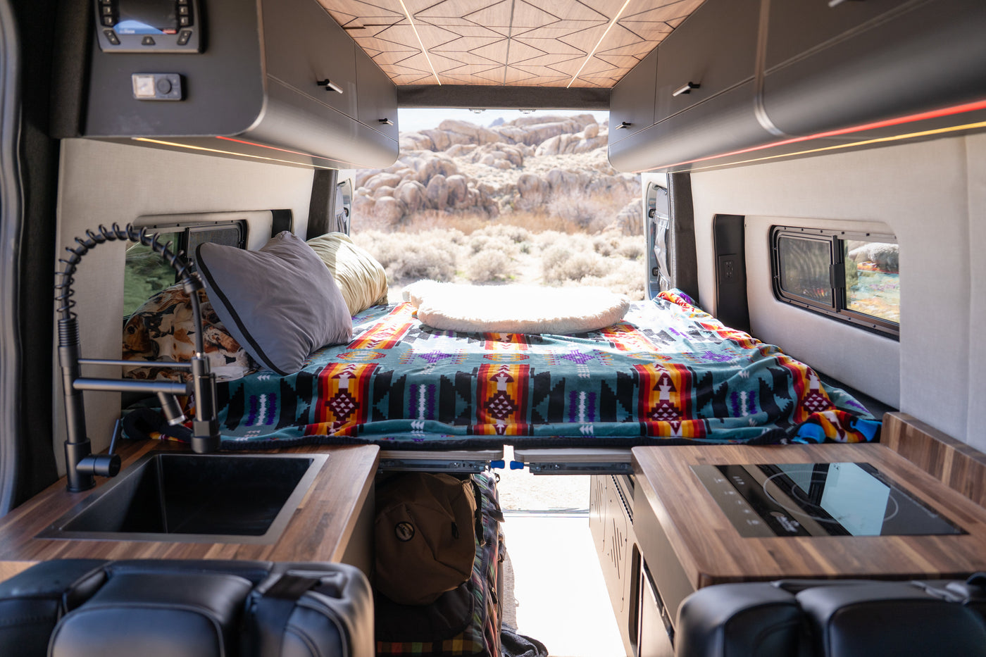 Inside a modern RV rental: comfy bed, compact kitchen, and open doors to a scenic desert view. Ideal for camper van adventures. — photo 3