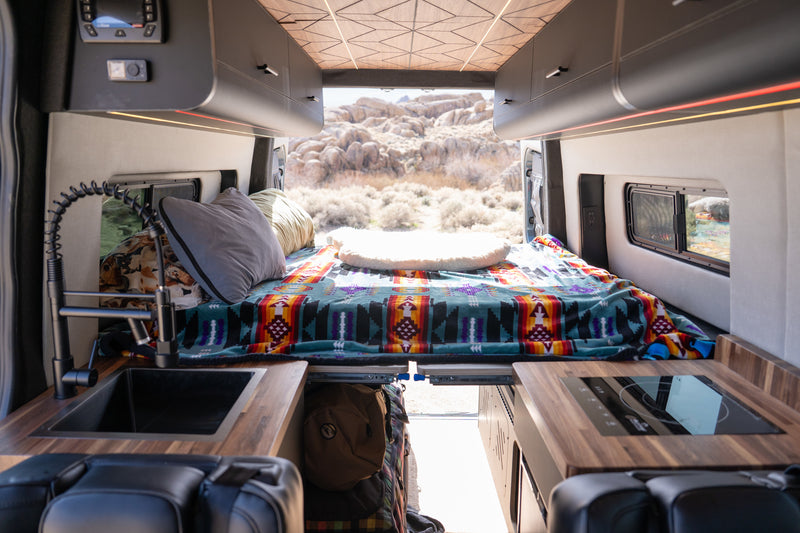 Inside a modern RV rental: comfy bed, compact kitchen, and open doors to a scenic desert view. Ideal for camper van adventures. — photo 3