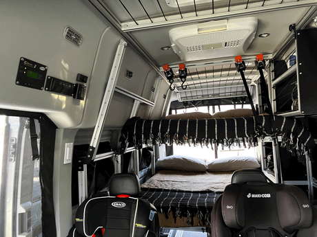 Explore family adventures in this RV rental! Interior view of a camper van featuring bunk beds and two child car seats for comfortable travel.