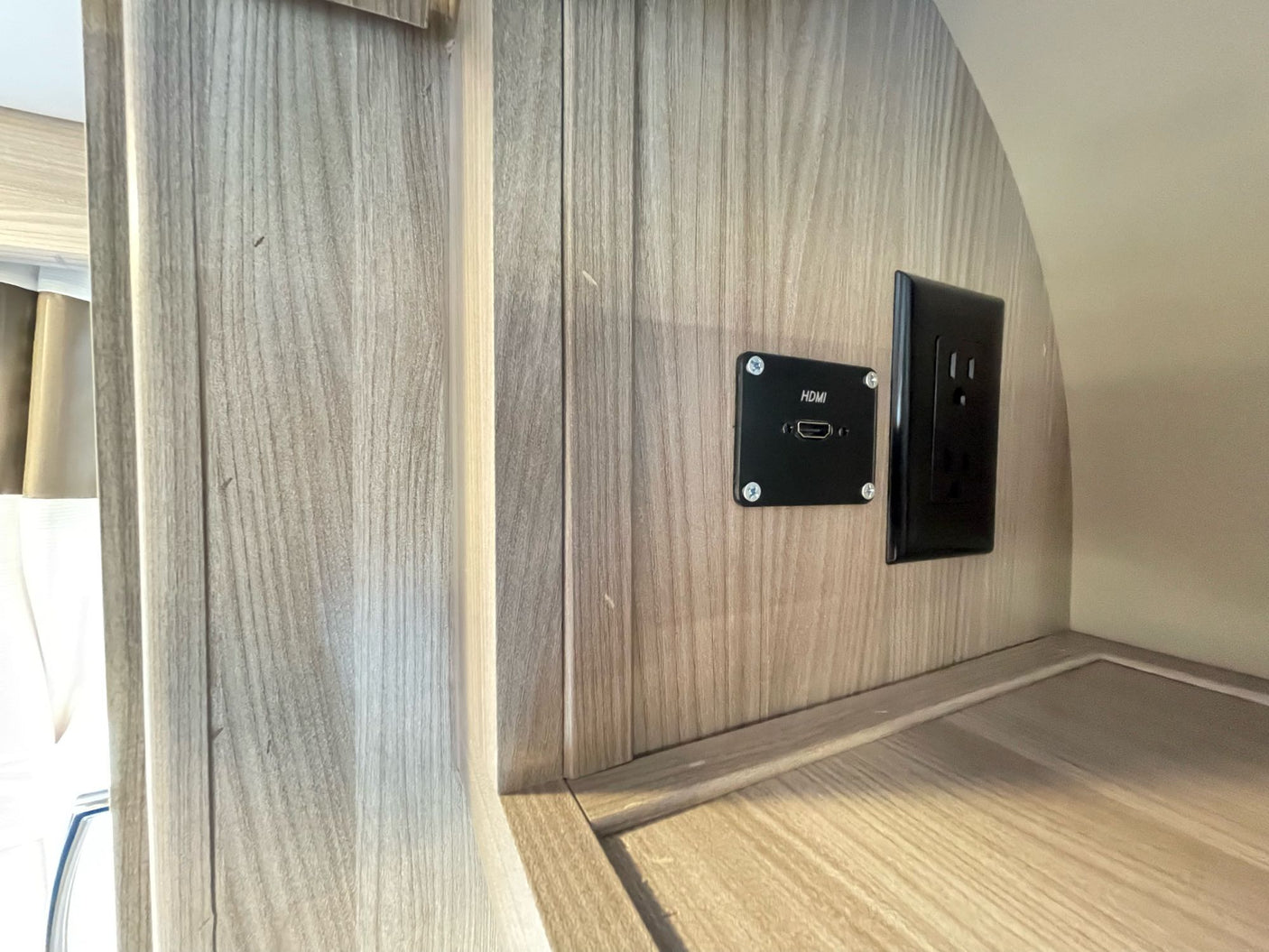RV rental entertainment hub: HDMI port and power outlet on a modern wood-look wall.