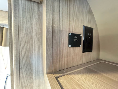 RV rental entertainment hub: HDMI port and power outlet on a modern wood-look wall.