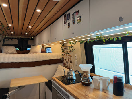 Cozy RV rental interior with a raised bed, compact kitchen, and fold-out table. Perfect for mobile living.