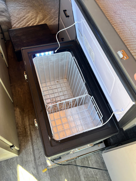 RV rental fridge: Interior view of an open portable freezer with two wire baskets and an LED light, ready for use.