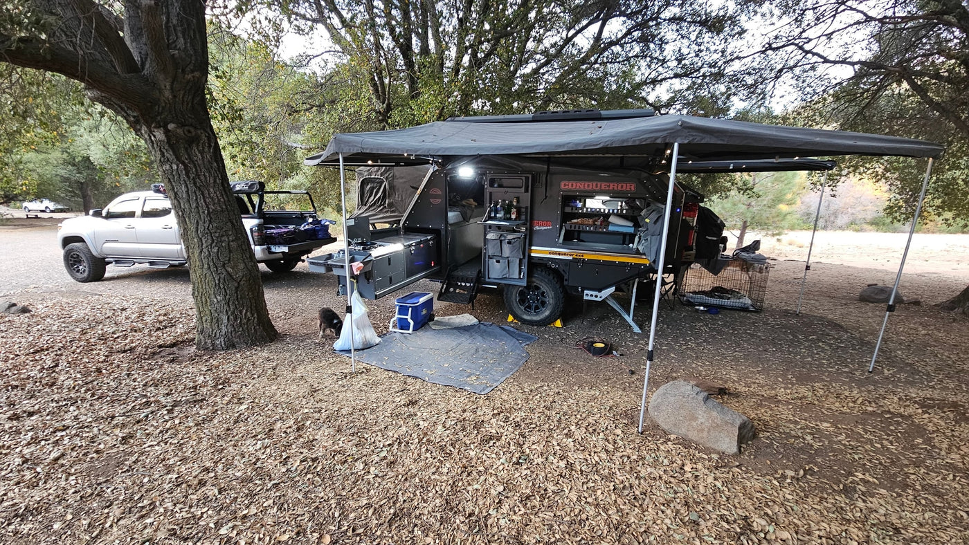Explore the wild with our RV rental! A truck & off-road camper trailer, complete with outdoor kitchen and awning, set up at a leafy campsite. — photo 16